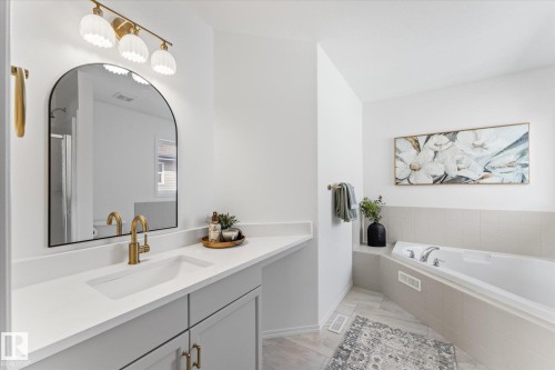 Contemporary bathroom featuring a spacious white countertop with an integrated sink, light-colored cabinetry with brass hardware, and a large arched mirror - 326 Silver Berry Road, Edmonton, AB - Indoor Photo Showing Bathroom