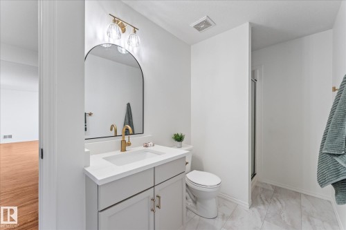 Contemporary bathroom featuring a light gray vanity with a white countertop, gold-finish faucet, and an arched wall mirror - 326 Silver Berry Road, Edmonton, AB - Indoor Photo Showing Bathroom