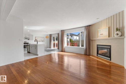 Spacious living area featuring polished wood-finish flooring, a contemporary fireplace with a mantel, and a large window providing ample natural light - 326 Silver Berry Road, Edmonton, AB - Indoor Photo Showing Living Room With Fireplace