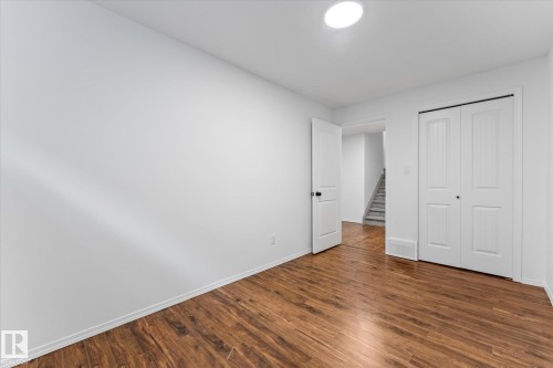 Room featuring wood-finish flooring, crisp white walls, a white interior door with black hardware, and a double bi-fold closet with vertical paneling - 326 Silver Berry Road, Edmonton, AB - Indoor Photo Showing Other Room