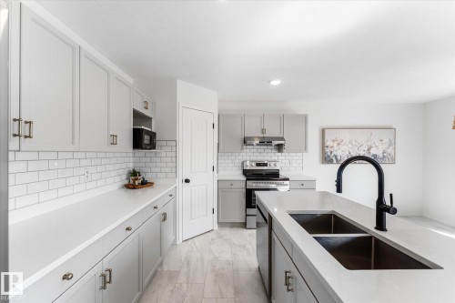 Modern kitchen featuring light gray cabinetry, white countertops, subway tile backsplash, stainless steel appliances, and a central island with a double basin sink and matte black faucet - 326 Silver Berry Road, Edmonton, AB - Indoor Photo Showing Kitchen With Double Sink With Upgraded Kitchen