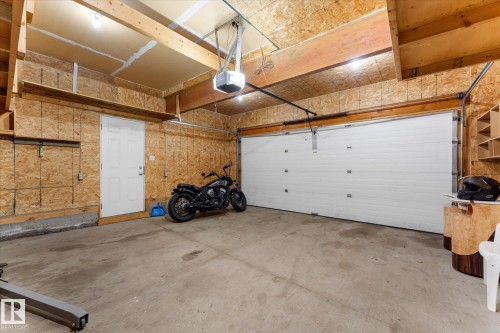Spacious garage featuring a concrete floor, a single white overhead door with an opener, a white entry door, visible wooden beams, and built-in shelving - 326 Silver Berry Road, Edmonton, AB - Indoor Photo Showing Garage