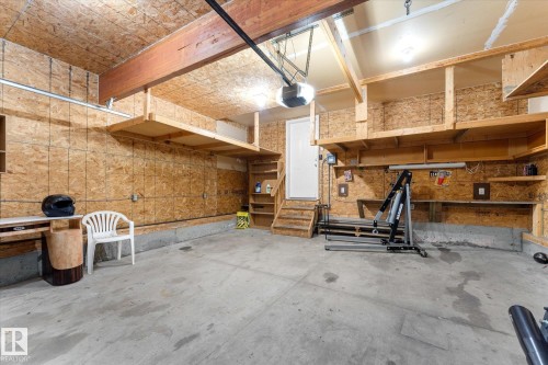 Garage space featuring a concrete floor, exposed wood beam ceiling, built-in shelving, and a pedestrian door with wood stairs - 326 Silver Berry Road, Edmonton, AB - Indoor