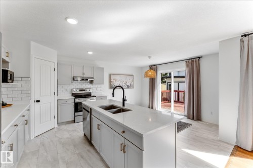Kitchen featuring a large central island with an undermount sink, light-toned cabinetry with gold-toned hardware, white subway tile backsplash, and stainless steel appliances - 326 Silver Berry Road, Edmonton, AB - Indoor Photo Showing Kitchen With Double Sink With Upgraded Kitchen