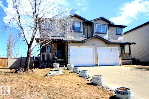 Two-story residence featuring light-toned siding, a double attached garage, multiple windows with dark trim, a covered front porch with railing, and a concrete driveway - 2927 30 Street, Edmonton, AB - Outdoor