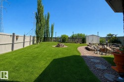 Expansive backyard featuring a manicured lawn, a stone pathway with stepping stones, a built-in fire pit area, and a rock garden with a water feature - 