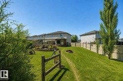 Expansive backyard featuring a tiered stone water feature, vibrant floral landscaping, a wood split-rail fence, a manicured lawn, and mature trees - 