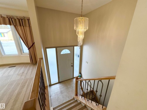 Entryway featuring a decorative chandelier, a front door with a frosted glass insert and side panel, and a staircase with a wooden handrail and wrought iron spindles - 8507 35 Avenue, Edmonton, AB - Indoor Photo Showing Other Room