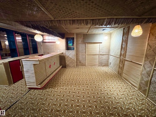 This room features a bar area with red cabinet doors, a patterned carpet, and walls and ceiling adorned with woven natural materials - 8507 35 Avenue, Edmonton, AB - Indoor