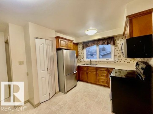 The kitchen features light-toned tiled flooring, wood cabinetry, stainless steel refrigerator, and a window with a valance - 8507 35 Avenue, Edmonton, AB - Indoor Photo Showing Kitchen With Double Sink