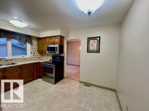 The kitchen features wood cabinetry, a stainless steel microwave and range, and tiled flooring - 8507 35 Avenue, Edmonton, AB - Indoor Photo Showing Kitchen