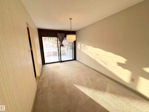 This room features neutral-toned carpet and walls, a ceiling-mounted light fixture, and a sliding glass door leading to an outdoor balcony with white railings - 8507 35 Avenue, Edmonton, AB - Indoor Photo Showing Other Room