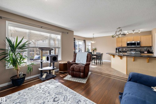 Open-concept living space featuring wood-finish flooring, a large window, and an adjacent kitchen with light wood cabinetry, stainless steel appliances, and a breakfast bar with a dark countertop - 992 Regency Drive, Sherwood Park, AB - Indoor Photo Showing Other Room