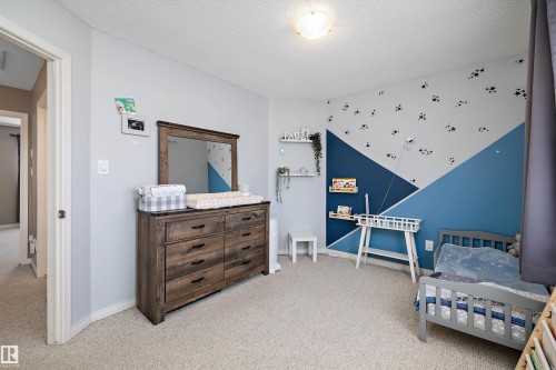 Carpeted interior room featuring light blue walls, a geometric accent wall with blue and gray tones, and a textured white ceiling - 992 Regency Drive, Sherwood Park, AB - Indoor Photo Showing Bedroom