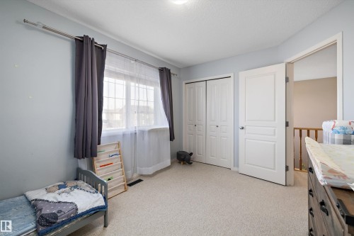 Carpeted room featuring a double window with grid pattern, neutral wall color, bifold closet doors, and a paneled entry door - 992 Regency Drive, Sherwood Park, AB - Indoor Photo Showing Bedroom