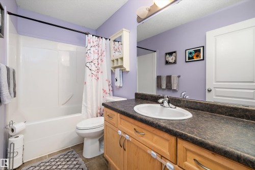 Full bathroom featuring a white tub/shower combination, a vanity with a white oval sink, wood-finish cabinetry, a dark countertop, and a large wall-mounted mirror - 992 Regency Drive, Sherwood Park, AB - Indoor Photo Showing Bathroom