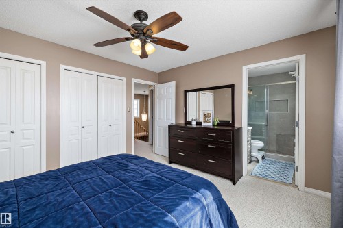 Carpeted bedroom featuring a ceiling fan with integrated lighting, two white bi-fold closet doors, and an en-suite bathroom with a glass-enclosed shower - 992 Regency Drive, Sherwood Park, AB - Indoor Photo Showing Bedroom