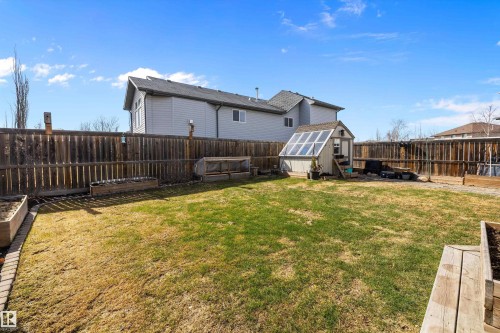 Expansive fenced backyard featuring a dedicated greenhouse structure, raised garden beds, and a wood privacy fence - 992 Regency Drive, Sherwood Park, AB - Outdoor With Exterior