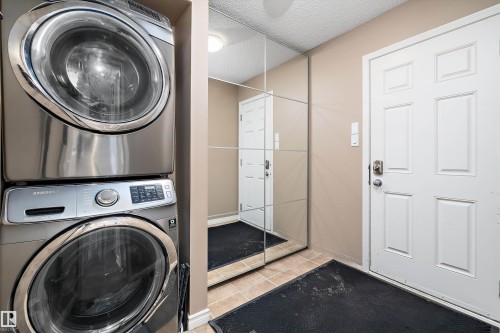 Integrated laundry area with stacked stainless steel washer and dryer, adjacent to mirrored closet doors - 992 Regency Drive, Sherwood Park, AB - Indoor Photo Showing Laundry Room
