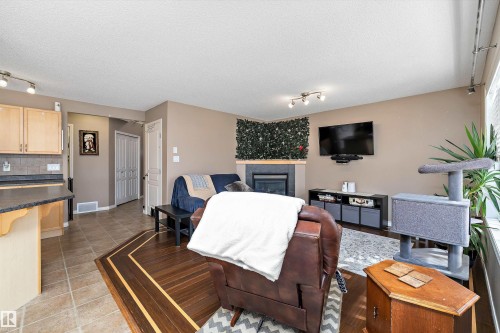 Living space featuring a fireplace with a decorative green panel, a wall-mounted television, and a track lighting fixture - 992 Regency Drive, Sherwood Park, AB - Indoor