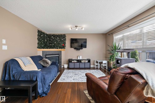 Living area featuring a floor-to-ceiling window with blinds, wood-finish flooring, a fireplace with a stone surround and wood mantel, and track lighting - 992 Regency Drive, Sherwood Park, AB - Indoor Photo Showing Living Room