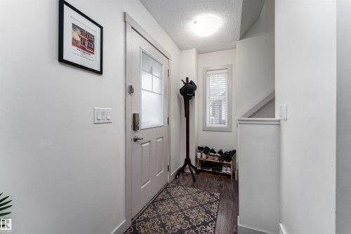 Entryway featuring a white paneled door with frosted glass, wood-finish flooring, a contemporary flush mount light fixture, and a window with horizontal blinds - 15 5203 149 Avenue, Edmonton, AB - Indoor Photo Showing Other Room