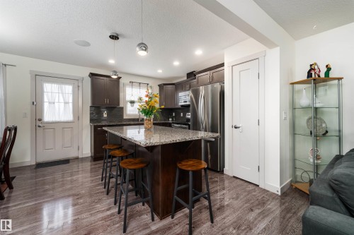 Kitchen featuring a central island with granite countertop, dark wood-finish cabinetry, stainless steel appliances, and wood-finish flooring - 15 5203 149 Avenue, Edmonton, AB - Indoor