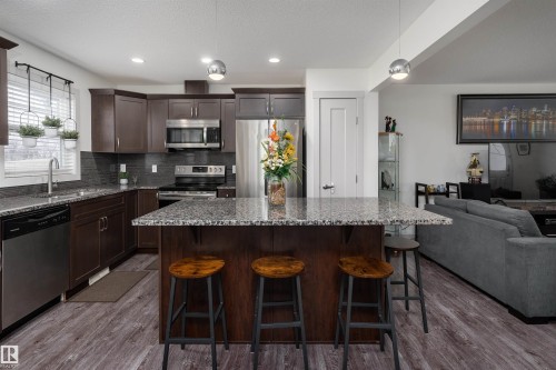 Kitchen featuring an island with stone-finish countertops, stainless steel appliances, dark wood-finish cabinetry, and wood-finish flooring - 15 5203 149 Avenue, Edmonton, AB - Indoor Photo Showing Kitchen With Double Sink With Upgraded Kitchen