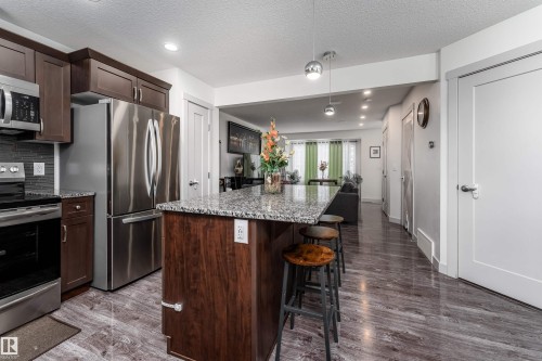 Kitchen featuring a granite-topped island with seating, stainless steel appliances, dark wood cabinetry, and a contrasting tile backsplash - 15 5203 149 Avenue, Edmonton, AB - Indoor Photo Showing Kitchen With Upgraded Kitchen