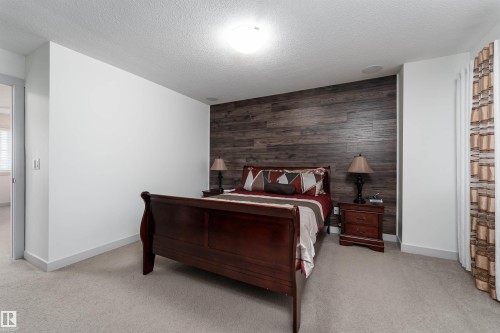 Bedroom featuring a wood-panel accent wall, recessed ceiling speaker, overhead lighting, and light-colored carpeting - 15 5203 149 Avenue, Edmonton, AB - Indoor Photo Showing Bedroom