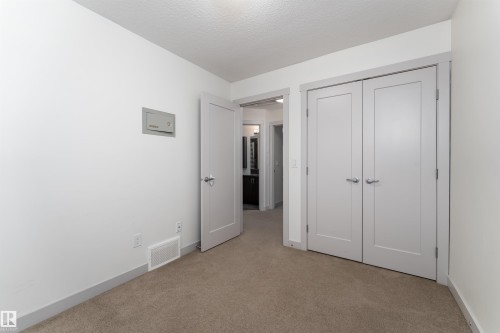 Neutral-toned carpeting extends throughout this interior space, featuring a double-door closet with brushed nickel hardware and a single interior door - 15 5203 149 Avenue, Edmonton, AB - Indoor Photo Showing Other Room