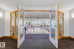 Double glass-paneled doors opening into a spacious communal area featuring a wood-finish dance floor, expansive window array, and wall-mounted sconces - 