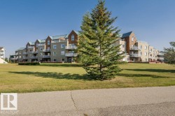 Multi-story residential building featuring light-toned exterior siding, numerous balconies with white railings, and dark-pitched rooflines - 