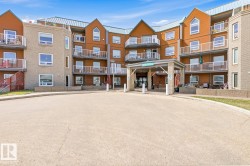 Multi-story building featuring a prominent covered entryway, multiple balconies with white railings, a mixed-material facade of brick and wood-finish siding, and a sloped metal roof - 