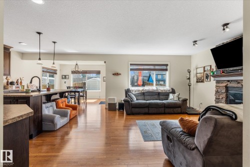 Open-concept living area featuring wood-finish flooring throughout, a stone-clad fireplace with a wood mantel, and large windows providing natural light - 41 Heron Crescent, Spruce Grove, AB - Indoor Photo Showing Living Room