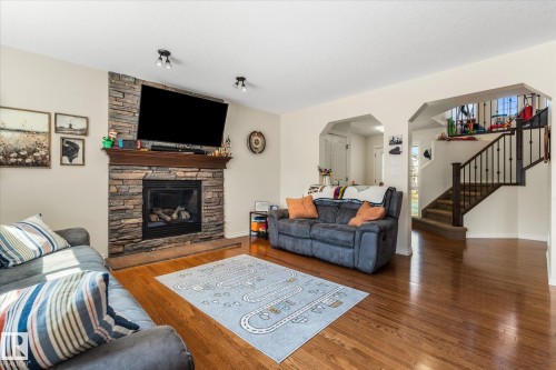 Living area featuring a floor-to-ceiling stacked stone fireplace with a wood mantle, hardwood flooring, recessed lighting, and an open staircase with wrought iron balusters - 41 Heron Crescent, Spruce Grove, AB - Indoor Photo Showing Living Room With Fireplace