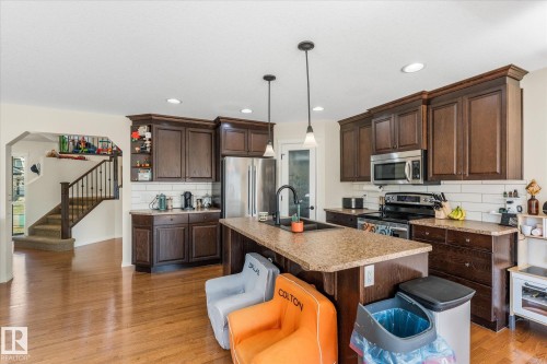 Kitchen featuring an island with a built-in sink, dark wood cabinetry, stainless steel appliances, subway tile backsplash, and recessed lighting - 41 Heron Crescent, Spruce Grove, AB - Indoor Photo Showing Kitchen With Double Sink With Upgraded Kitchen