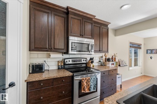 Kitchen featuring rich wood cabinetry, stainless steel appliances, stone-finish countertops, and a white subway tile backsplash - 41 Heron Crescent, Spruce Grove, AB - Indoor Photo Showing Kitchen