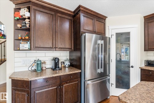 Kitchen featuring dark wood-finish cabinetry, light speckled countertops, a white subway tile backsplash, and a stainless steel French door refrigerator - 41 Heron Crescent, Spruce Grove, AB - Indoor Photo Showing Kitchen