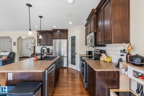 Kitchen featuring rich wood cabinetry, stainless steel appliances, a center island with pendant lighting, a black undermount sink with a gooseneck faucet, and wood-finish flooring - 41 Heron Crescent, Spruce Grove, AB - Indoor Photo Showing Kitchen With Double Sink With Upgraded Kitchen