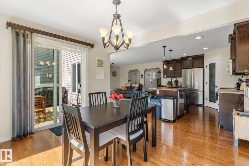 Open-concept dining area featuring wood-finish flooring, a sliding glass door to an exterior deck, and a chandelier light fixture - 41 Heron Crescent, Spruce Grove, AB - Indoor Photo Showing Dining Room