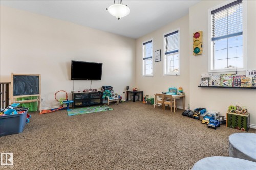 Carpeted room featuring high ceilings, multiple windows with blinds, a wall-mounted television, built-in shelving, and a ceiling-mounted light fixture - 41 Heron Crescent, Spruce Grove, AB - Indoor