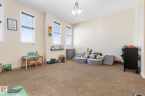 Spacious room featuring neutral carpeting, multiple windows with blinds, a wall-mounted light fixture, and a built-in floating shelf - 41 Heron Crescent, Spruce Grove, AB - Indoor