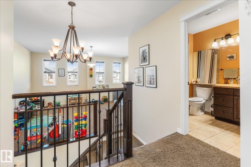 Upper-level landing featuring a chandelier, a private bathroom with a dark wood vanity, a toilet, a shower with a striped curtain, and tile flooring - 41 Heron Crescent, Spruce Grove, AB - Indoor Photo Showing Other Room