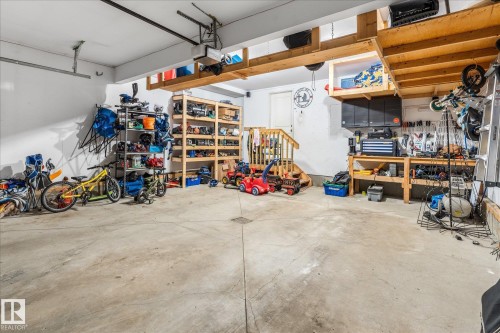 Concrete floor garage featuring built-in wooden shelving, overhead storage, a workbench area, and a staircase with wooden railings - 41 Heron Crescent, Spruce Grove, AB - Indoor Photo Showing Garage