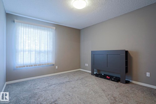 Carpeted room featuring neutral-toned walls, white baseboards, and a window with vertical blinds - 201 1520 Hammond Gate Gate, Edmonton, AB - Indoor Photo Showing Other Room