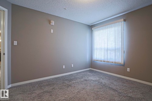 Carpeted room featuring a window with vertical blinds, neutral wall paint, white trim, and a textured ceiling - 201 1520 Hammond Gate Gate, Edmonton, AB - Indoor Photo Showing Other Room