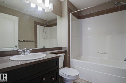 Bathroom featuring a dark wood-finish vanity with an integrated sink, polished chrome faucet, and expansive wall-mounted mirror - 201 1520 Hammond Gate Gate, Edmonton, AB - Indoor Photo Showing Bathroom