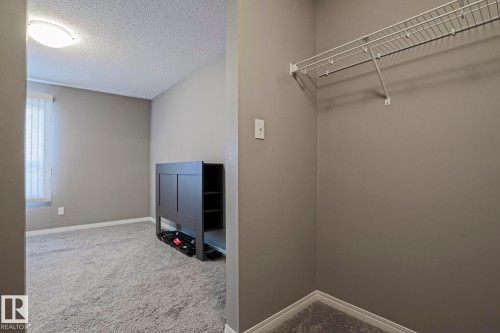 Spacious room featuring neutral carpeting, light gray walls, a window with vertical blinds, and a flush-mount ceiling light fixture - 201 1520 Hammond Gate Gate, Edmonton, AB - Indoor Photo Showing Other Room