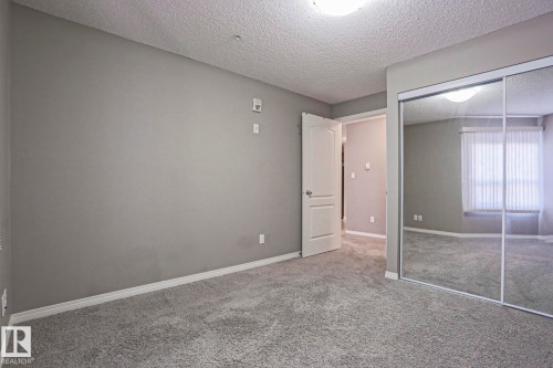 Carpeted room featuring light gray walls, white trim, a mirrored closet, and a ceiling-mounted light fixture - 201 1520 Hammond Gate Gate, Edmonton, AB - Indoor Photo Showing Other Room
